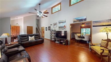 Living area featuring a ceiling fan, high vaulted ceiling, wood finished floors, and stairs
