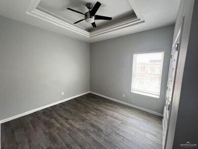 Empty room with dark hardwood / wood-style flooring, ceiling fan, and a raised ceiling