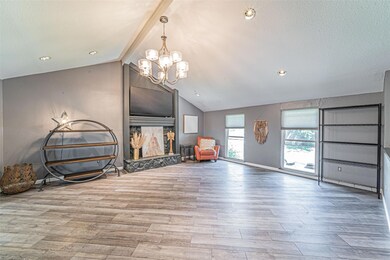 Living room with a textured ceiling, lofted ceiling with beams, a fireplace, an inviting chandelier, and hardwood / wood-style flooring