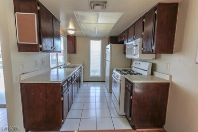 Kitchen featuring white appliances, light countertops, light tile patterned floors, and dark brown cabinetry