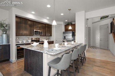 Kitchen featuring stainless steel appliances, wine cooler, a kitchen breakfast bar, light wood-style flooring, and backsplash