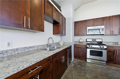 Kitchen featuring appliances with stainless steel finishes, light stone countertops, concrete floors, and dark brown cabinets