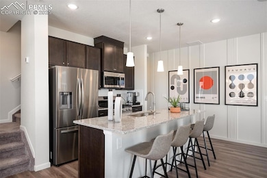 Kitchen with appliances with stainless steel finishes, a sink, dark brown cabinets, wood finished floors, and a kitchen island with sink