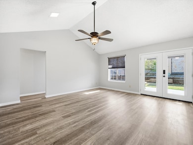 Empty room featuring vaulted ceiling, light wood-type flooring, a textured ceiling, french doors, and ceiling fan