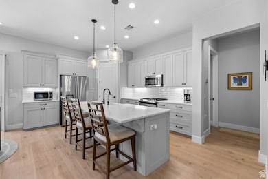 Kitchen with a kitchen bar, decorative backsplash, light wood-style flooring, stainless steel appliances, and recessed lighting