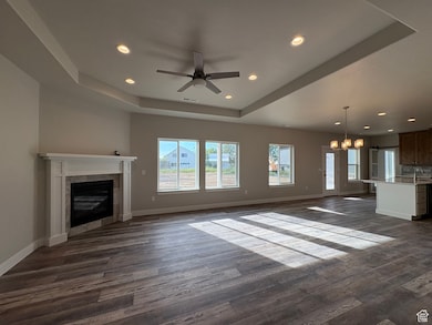Unfurnished living room with a tray ceiling, a chandelier, recessed lighting, dark wood-type flooring, and a tiled fireplace