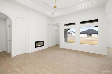 Unfurnished living room featuring ornamental molding, light hardwood / wood-style flooring, a raised ceiling, and a towering ceiling