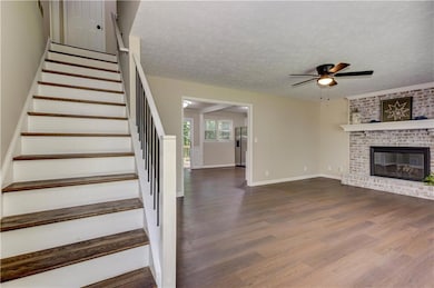 Stairs with wood finished floors, ceiling fan, a textured ceiling, and a brick fireplace