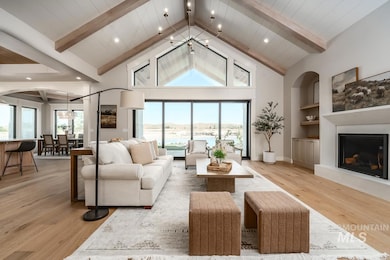Living area featuring light wood finished floors, a fireplace with raised hearth, beam ceiling, high vaulted ceiling, and a chandelier