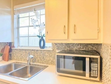 Kitchen view of stainless steel microwave, tasteful backsplash, light countertops, and white cabinets