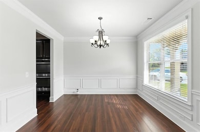 Unfurnished dining area with wainscoting, a decorative wall, ornamental molding, dark wood-type flooring, and a chandelier