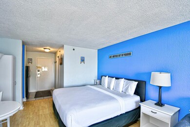 Bedroom with light wood-style floors, a textured ceiling, and freestanding refrigerator