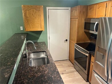 Kitchen with stainless steel appliances, sink, dark stone countertops, and light wood-type flooring