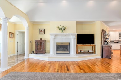 Living area with wood finished floors, arched walkways, ornamental molding, ornate columns, and a tiled fireplace