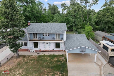 View of front facade featuring a balcony, a chimney, driveway, a carport, and roof with shingles