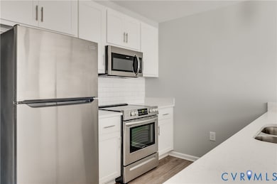 Kitchen with stainless steel appliances, white cabinetry, backsplash, light wood finished floors, and light stone countertops