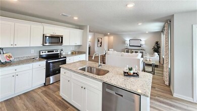 Kitchen with white cabinetry, stainless steel appliances, light wood-style flooring, light stone countertops, and a kitchen island with sink