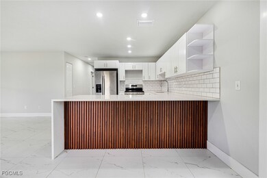 Kitchen with open shelves, white cabinets, a peninsula, appliances with stainless steel finishes, and light stone counters