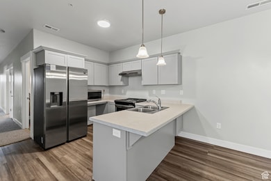 Kitchen featuring light countertops, appliances with stainless steel finishes, a peninsula, decorative light fixtures, and gray cabinetry