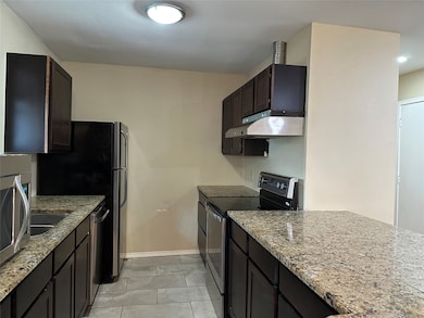 Kitchen with stainless steel appliances, light stone counters, under cabinet range hood, and light tile patterned flooring