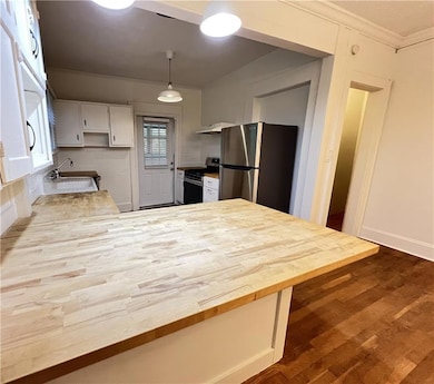 Kitchen with a peninsula, dark wood-type flooring, white cabinetry, appliances with stainless steel finishes, and wood counters