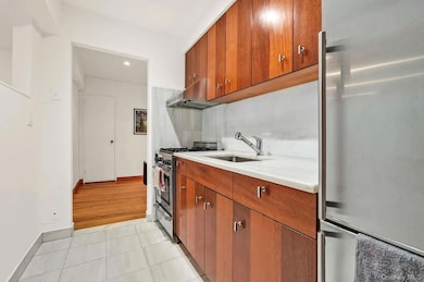 Kitchen with stainless steel appliances, brown cabinetry, light tile patterned flooring, ventilation hood, and recessed lighting