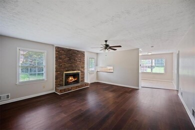 Unfurnished living room featuring a textured ceiling, wood finished floors, a brick fireplace, baseboards, and a ceiling fan