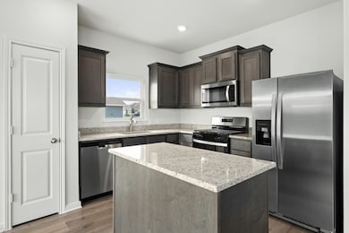 Kitchen featuring stainless steel appliances, dark brown cabinets, light stone counters, dark wood finished floors, and a center island