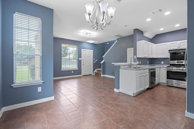 Kitchen featuring appliances with stainless steel finishes, a sink, a chandelier, white cabinetry, and a peninsula