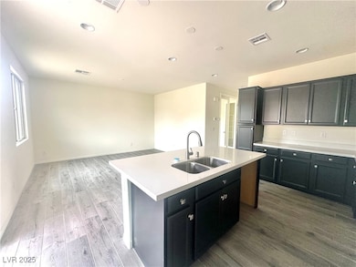 Kitchen with dark cabinetry, light countertops, dark wood-style floors, an island with sink, and recessed lighting