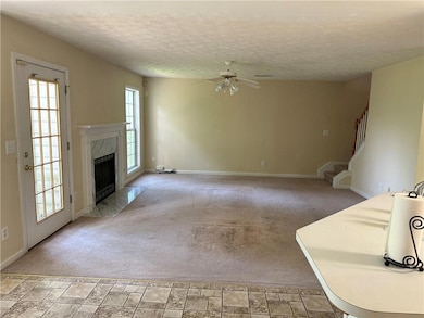 Unfurnished living room with ceiling fan, a textured ceiling, a premium fireplace, stairway, and baseboards