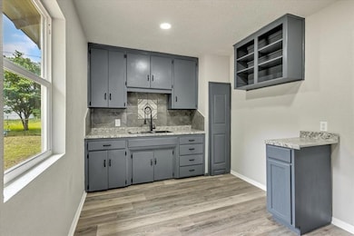 Kitchen featuring a sink, gray cabinetry, decorative backsplash, open shelves, and light countertops