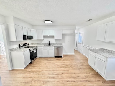 Kitchen with light wood-style floors, appliances with stainless steel finishes, a textured ceiling, white cabinets, and light stone counters