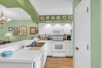 Kitchen with white appliances, a peninsula, light wood finished floors, white cabinetry, and recessed lighting