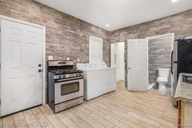 Kitchen featuring tile walls, stainless steel appliances, light wood-type flooring, washer and dryer, and light countertops