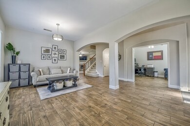 Living room with arched walkways, an office area, stairway, and light wood finished floors