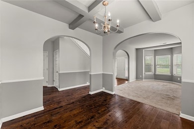 Empty room with beam ceiling, wood-type flooring, baseboards, a chandelier, and arched walkways