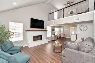 Living room with a ceiling fan, high vaulted ceiling, a brick fireplace, beam ceiling, and wood finished floors