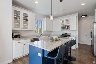 Kitchen featuring glass insert cabinets, light stone countertops, a breakfast bar, white cabinets, and recessed lighting