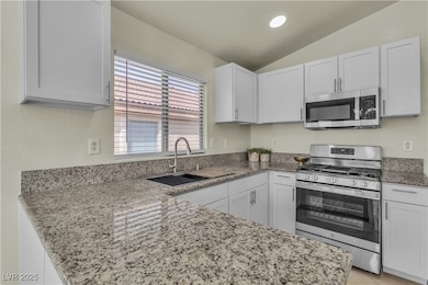 Kitchen featuring stainless steel appliances, light stone countertops, lofted ceiling, white cabinets, and a peninsula