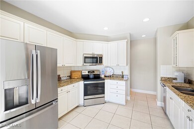 Kitchen featuring appliances with stainless steel finishes, tasteful backsplash, white cabinets, glass insert cabinets, and light stone counters