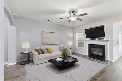 Living area featuring light wood-style flooring, a glass covered fireplace, ceiling fan, and arched walkways