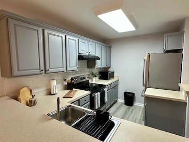 Kitchen with appliances with stainless steel finishes, gray cabinets, under cabinet range hood, backsplash, and light wood finished floors
