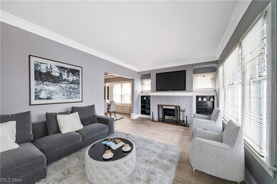 Living room virtually staged with ornamental molding, a brick fireplace, and light hardwood floors
