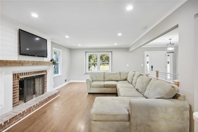 Living room with light hardwood / wood-style flooring, crown molding, and a brick fireplace