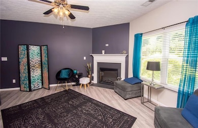 Living room featuring a textured ceiling, wood finished floors, ceiling fan, and a fireplace
