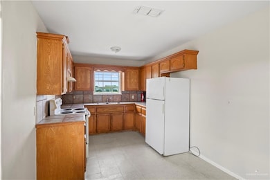 Kitchen with white appliances, brown cabinetry, backsplash, tile counters, and under cabinet range hood