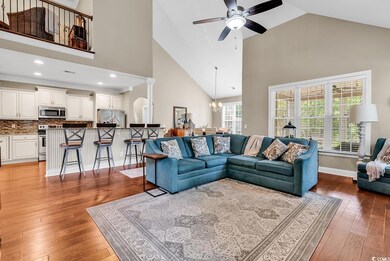 Living room featuring high vaulted ceiling, ceiling fan, a chandelier, light wood-style floors, and baseboards