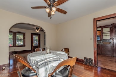 Dining room with dark wood-style floors, arched walkways, and ceiling fan
