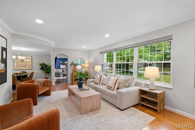Living area featuring light wood finished floors, arched walkways, ornamental molding, recessed lighting, and a chandelier
